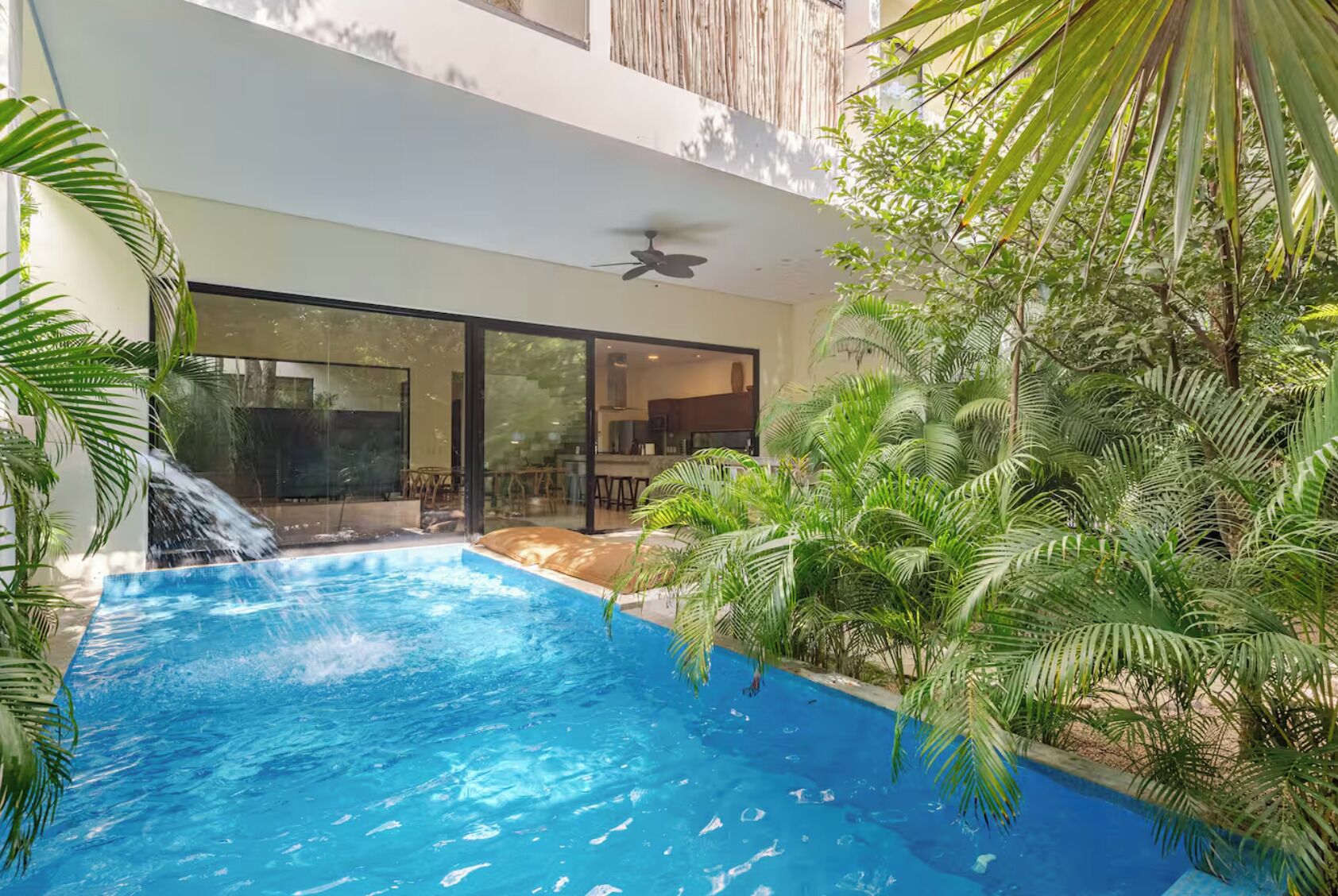 An indoor swimming pool with a waterfall feature, surrounded by lush greenery and modern architecture.