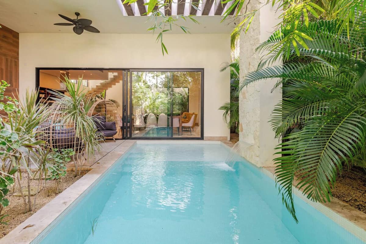 A swimming pool with a glass enclosure, surrounded by tropical plants and a wooden deck.