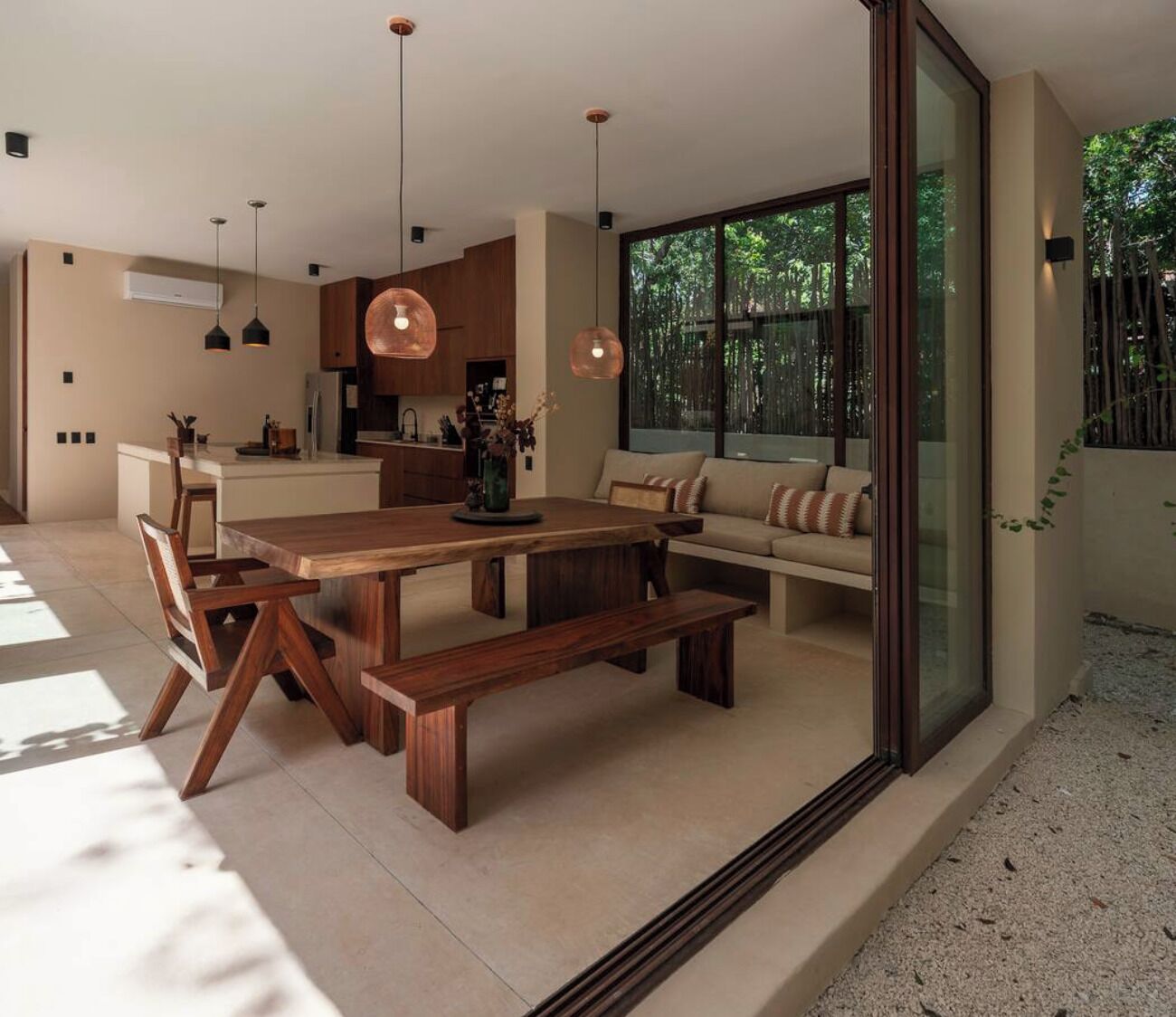 Una cucina moderna con isola centrale, un'area pranzo con tavolo e panche in legno, e un'ampia porta vetrata scorrevole che dà su un giardino.