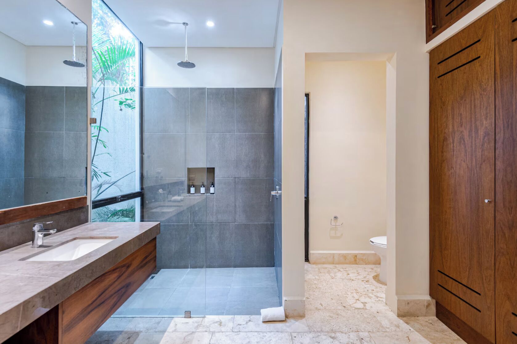 A modern bathroom with a large mirror, two sinks, a shower area, and wooden cabinets.
