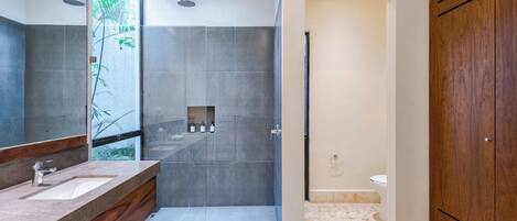 A modern bathroom with a large mirror, two sinks, a shower area, and wooden cabinets.