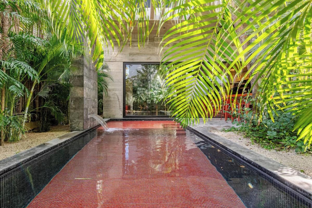 A pool area with a red tiled floor, surrounded by lush greenery and palm trees.