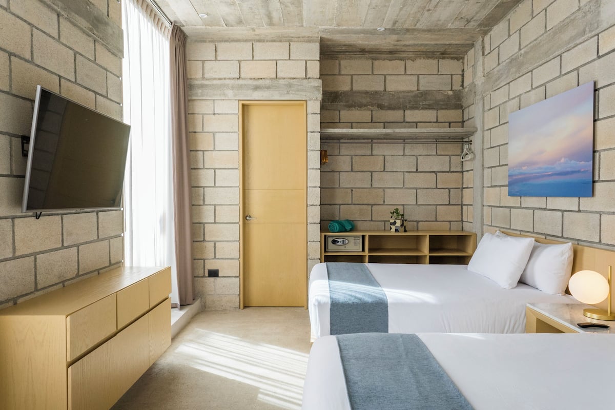 A hotel room with two beds, a TV, a wooden dresser, a desk, and a painting on the wall.