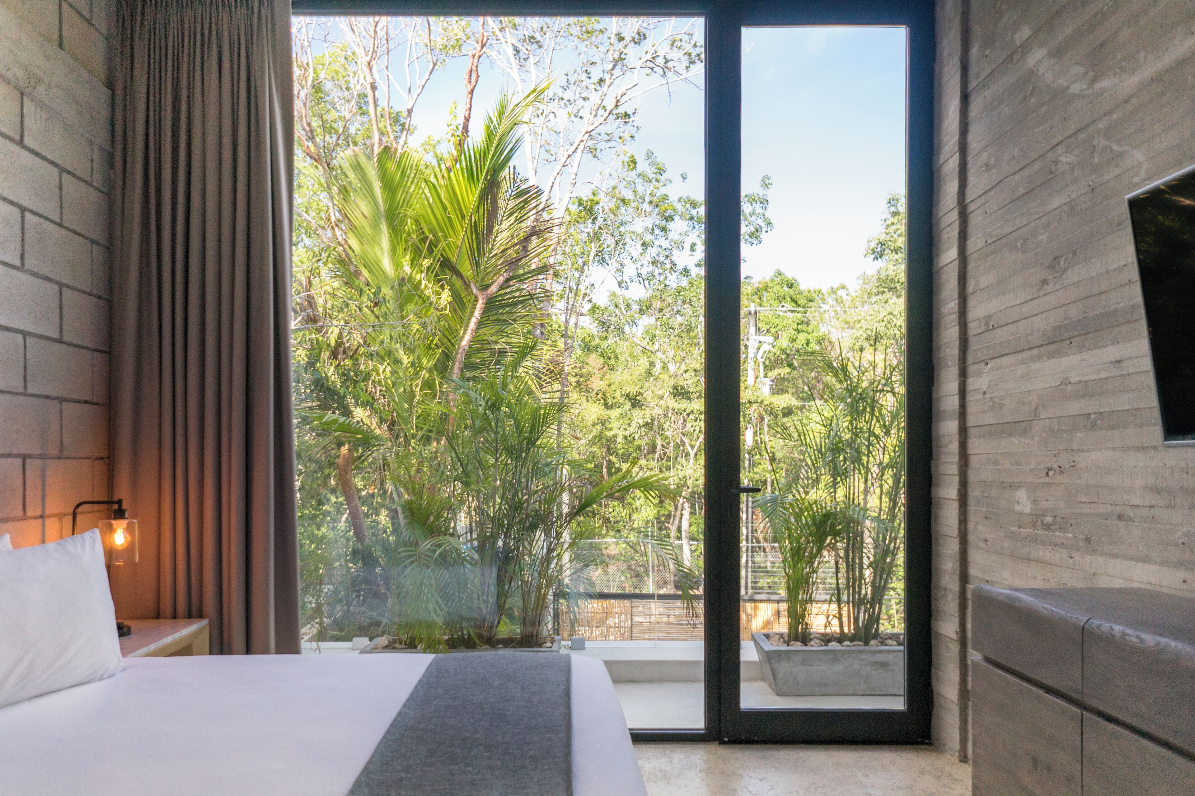 A bedroom with a bed, a nightstand, a lamp, a sliding glass door to a balcony, and a TV on the wall.