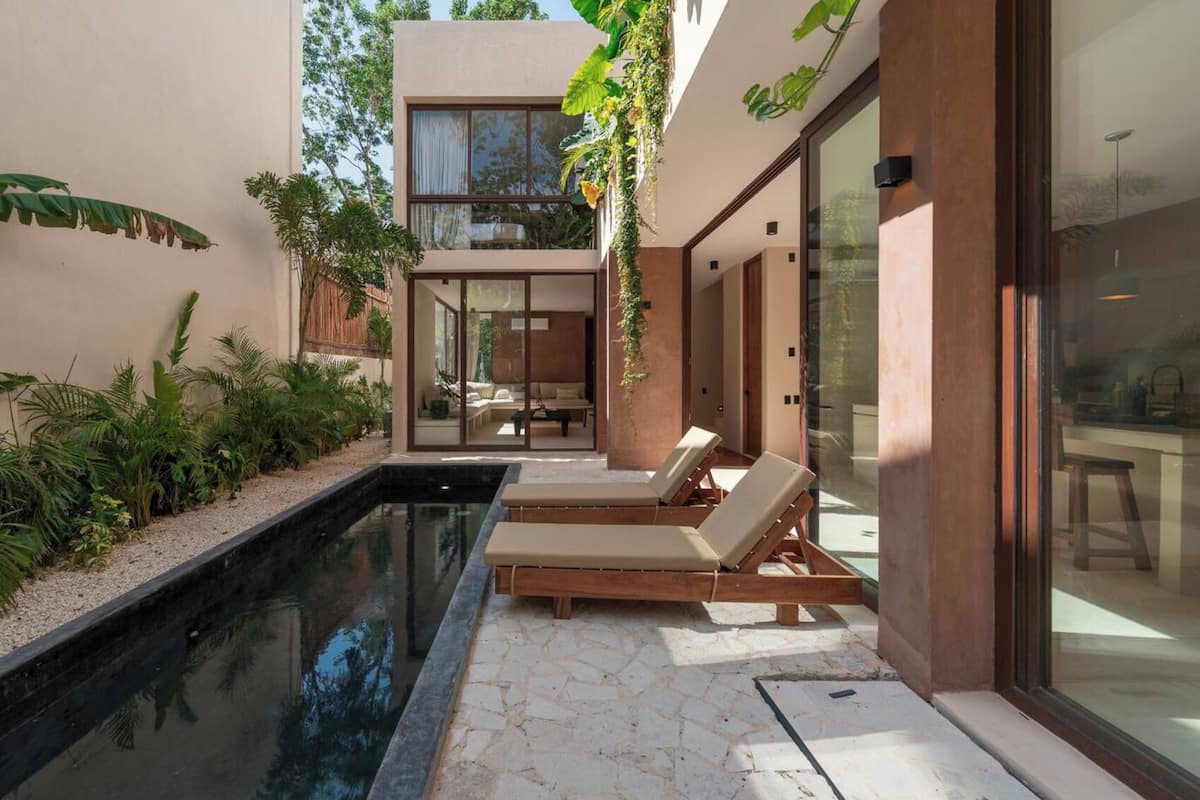 A modern outdoor pool area with lounge chairs, a glass-enclosed patio, and lush greenery.