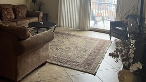 A living room with a brown sofa, a coffee table, a patterned rug, a ceiling fan, and a view of buildings through a large window with white curtains. - 3 beds 3 baths and amazing views of Jordan Hare!! (Auburn)