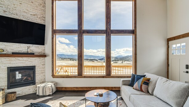 A living room with a fireplace, a large window with a view of mountains, and a cozy seating area. - 'Meadowlark Mountain Club' w/ Views of the Rockies (Jefferson)
