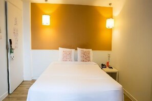 Une chambre d’hôtel comprenant un lit, une table de chevet et deux lampes fixées au mur.
