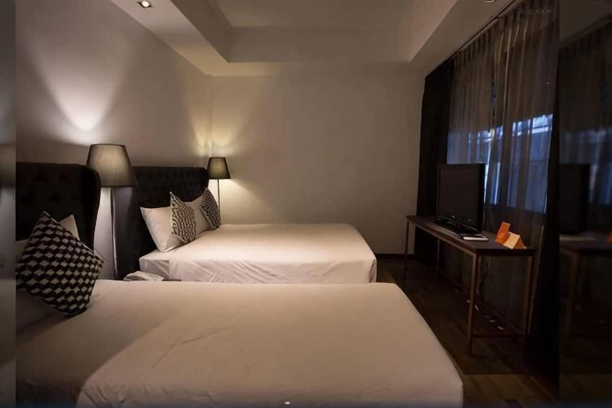 A hotel room with two beds, a desk, a TV, and a window with curtains.