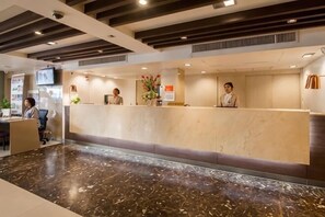 A hotel reception area with a marble reception desk, a TV screen, and a plant.