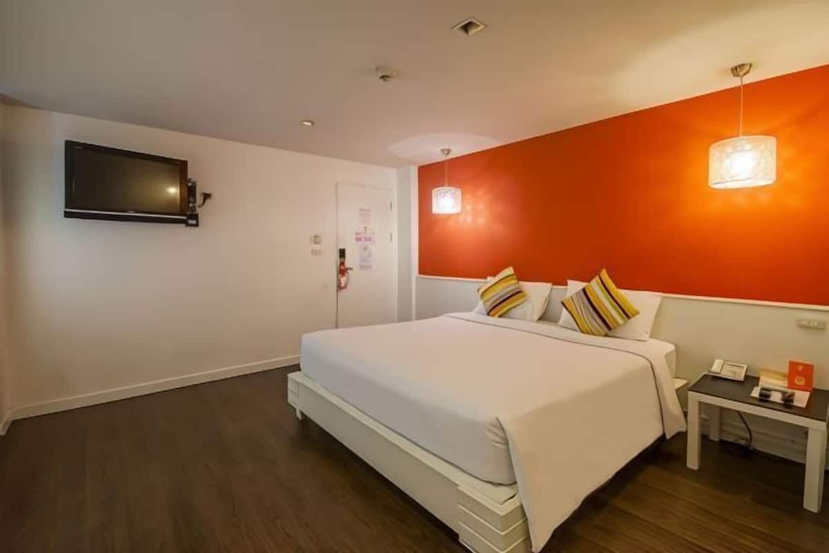 A hotel room with a bed, a bedside table with a phone, a wall-mounted TV, and a door with a lock.