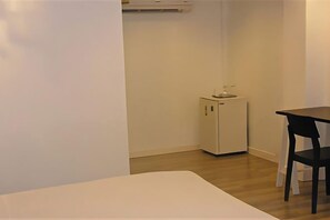 A small room with a white bed, a white cabinet, a black chair, and a wooden floor. - First House Hotel Bangkok (Bangkok)