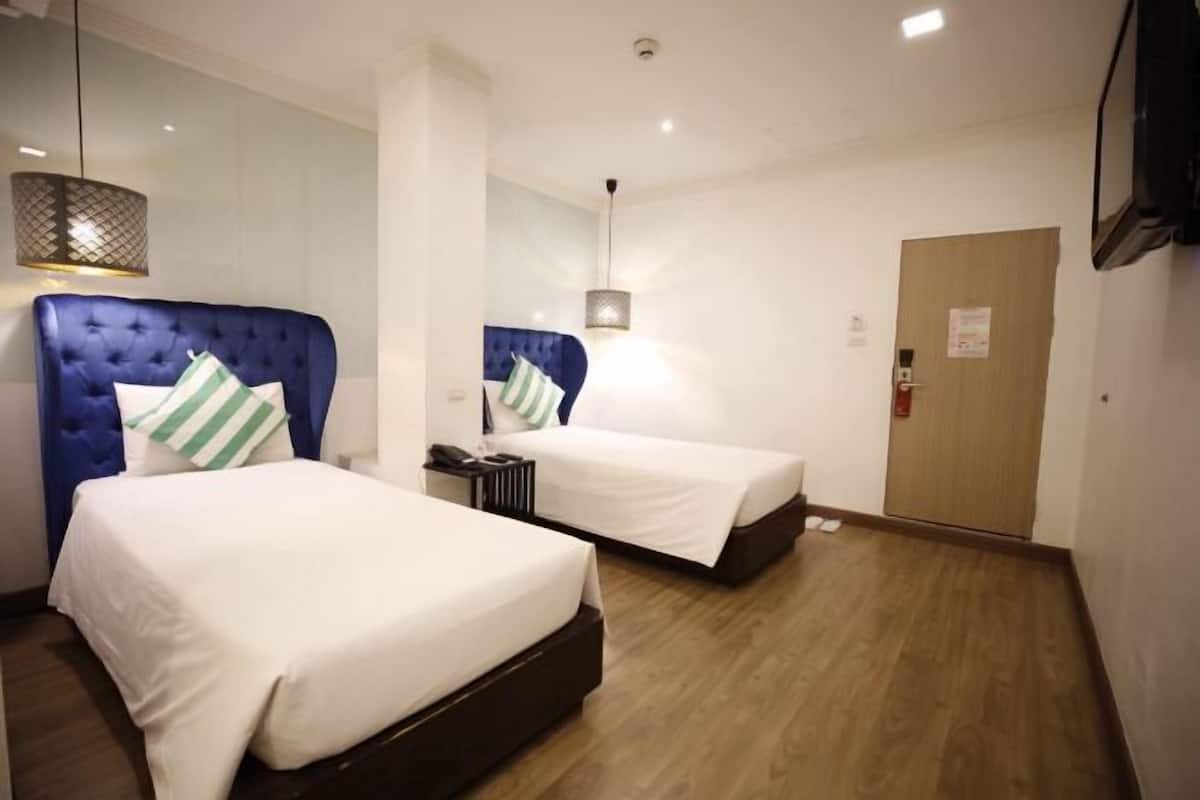 A hotel room with two beds, a wooden floor, a wardrobe, and a hanging light fixture.