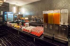 A hotel bar with multiple beverage dispensers, a coffee machine, and a tray of glasses.