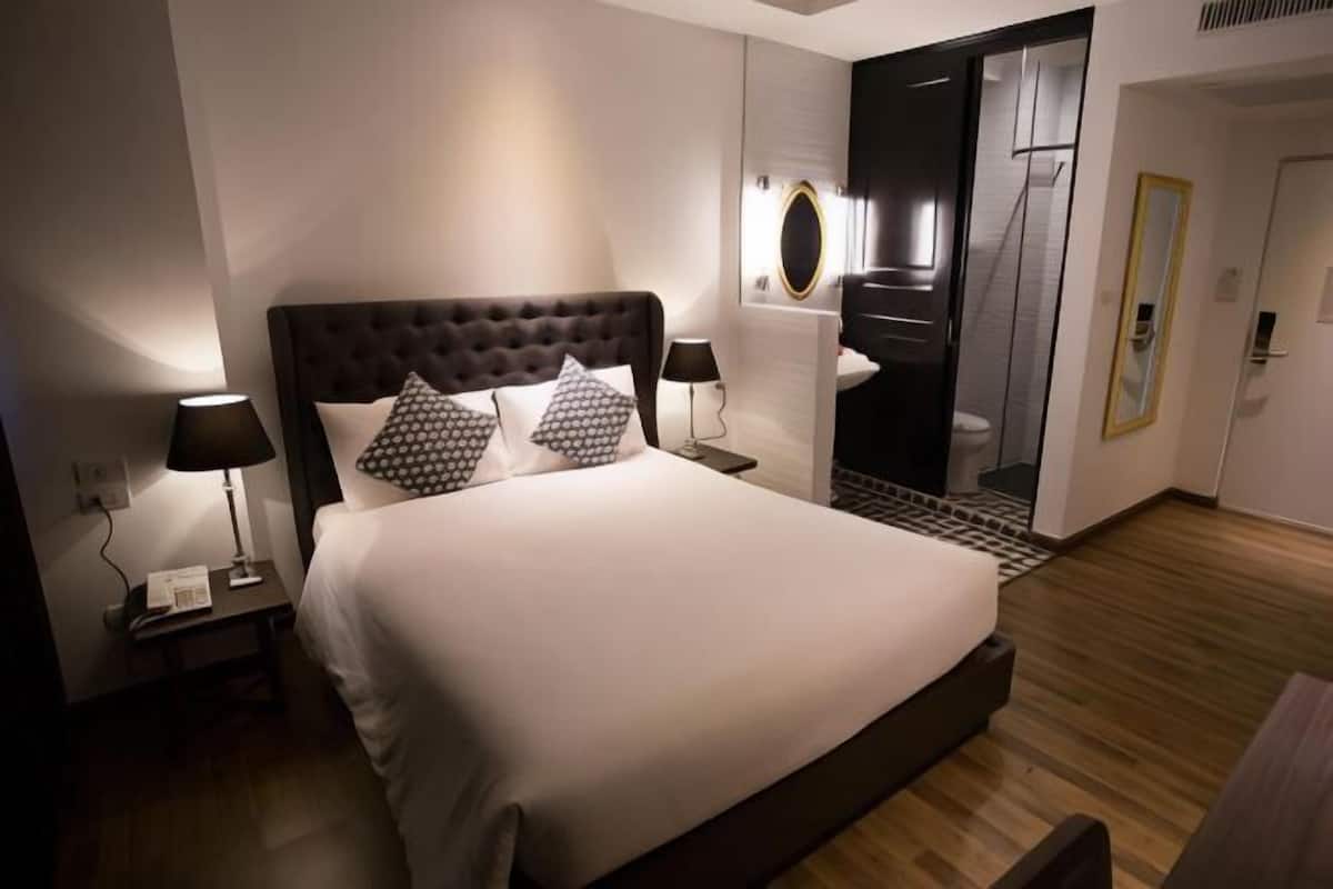 A modern hotel room with a large bed, two bedside tables with lamps, a mirror, and a wooden floor.