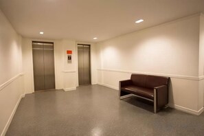 A hallway with two elevators, a bench, and a fire alarm. - First House Hotel Bangkok (Bangkok)
