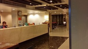 Zona de recepción de hotel con suelo de mármol, mostrador de recepción, un reloj y una escalera al fondo.