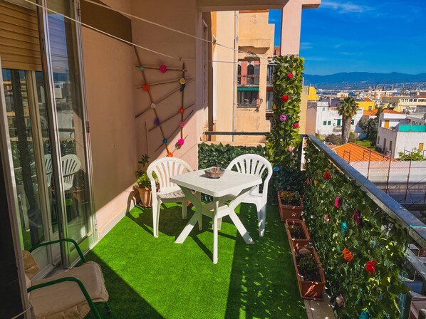 A balcony with a small table and chairs, potted plants, and a view of the cityscape.