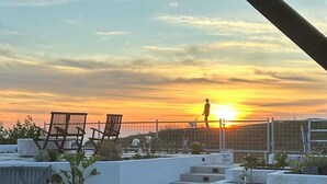 A rooftop terrace with a view of the sunset, a person walking, and several lounge chairs. - Ocean Mountain Island Views Guesthouse Along Trail (Ventura)