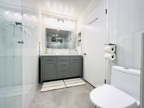 Un baño moderno con cabina de ducha de vidrio, un mueble de tocador gris con espejo y un inodoro con papel higiénico.