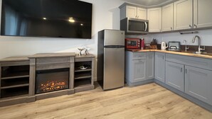 A modern kitchen with grey cabinets, a stainless steel refrigerator, a microwave, a red toaster oven, and a flat-screen TV mounted on the wall. - Ocean Mountain Island Views Guesthouse Along Trail (Ventura)