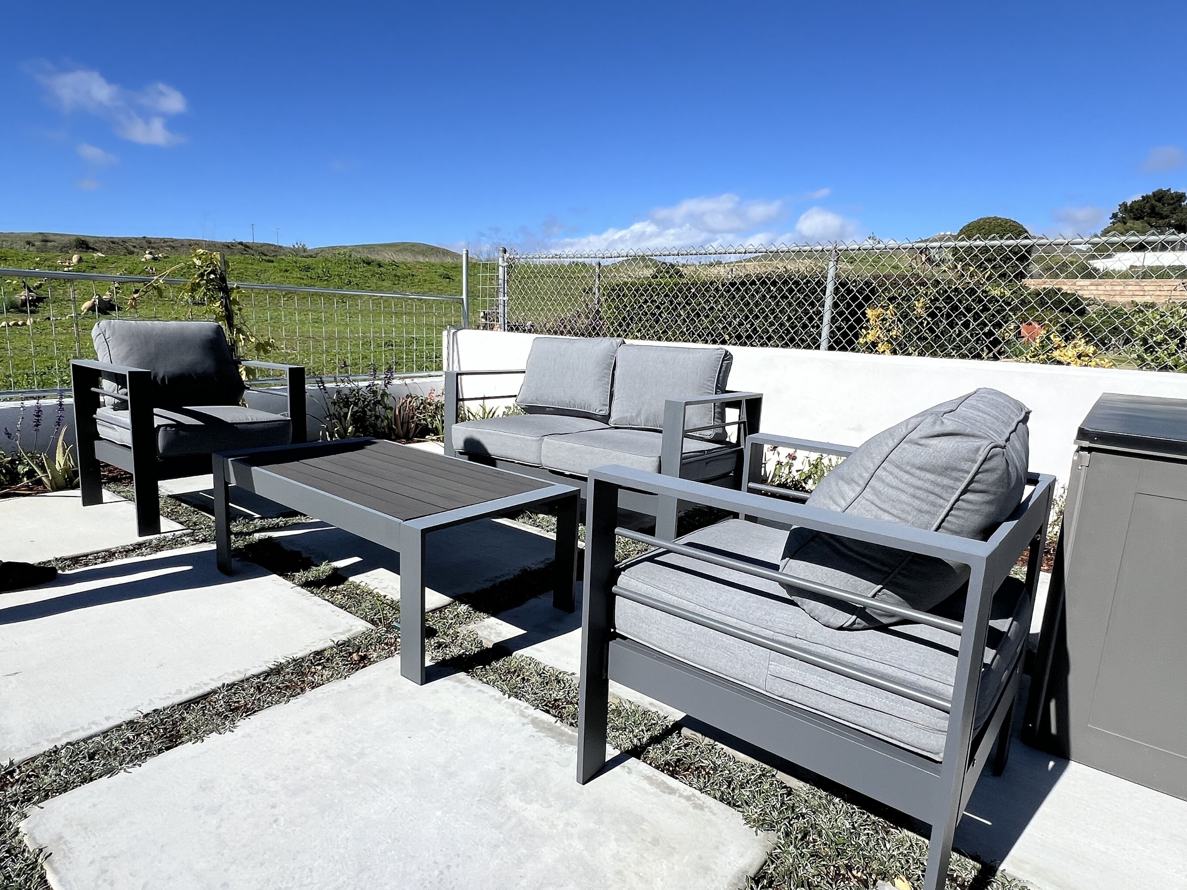 An outdoor patio with a grey sofa, two armchairs, and a small table.