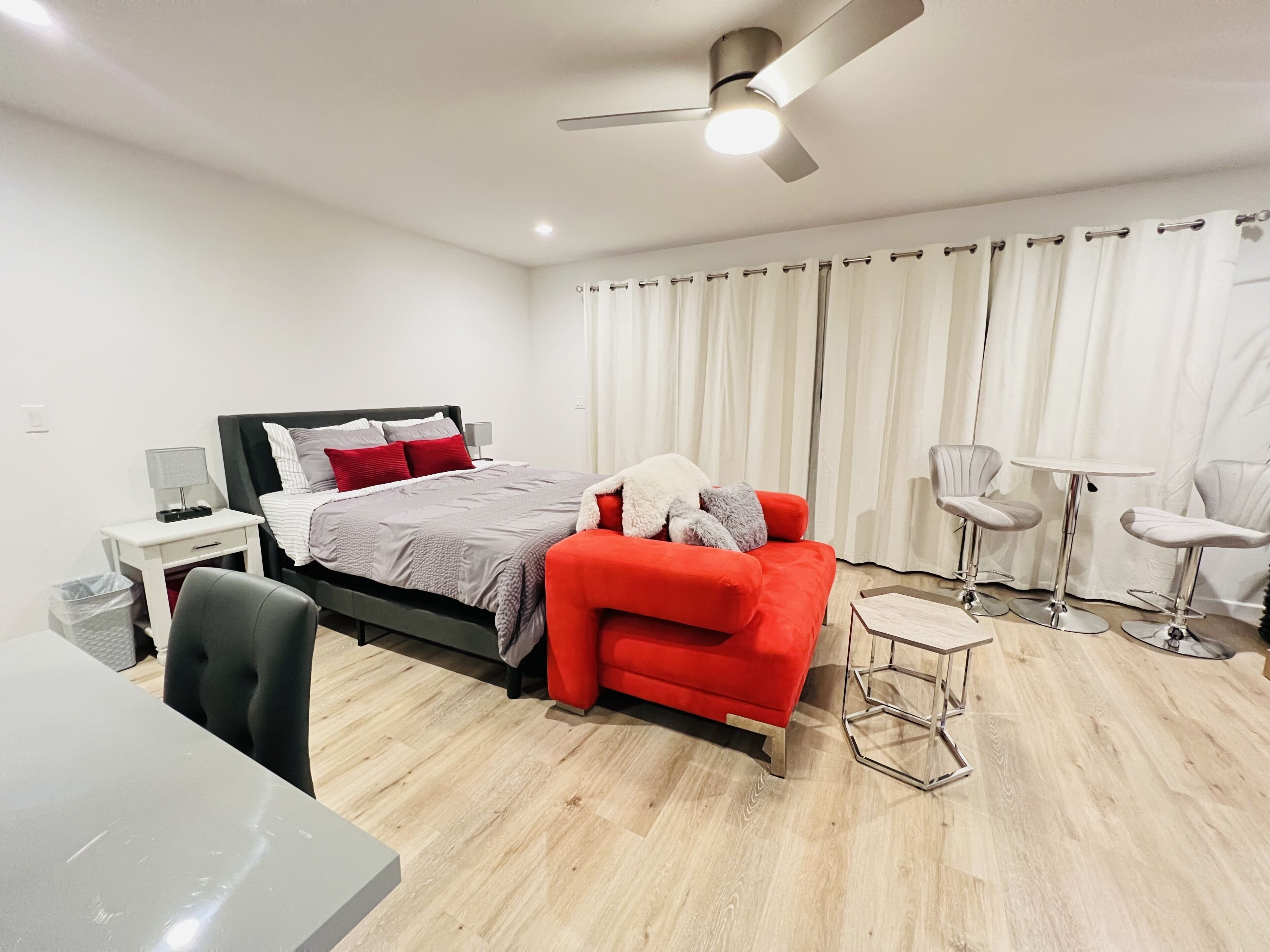 Un dormitorio moderno con una cama, un sofá rojo, un escritorio y un ventilador de techo.
