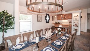 A dining area with a wooden table set for six, a chandelier, and a view into the kitchen. - Havasu Whaler -  Pool, Spa, Game Room, Casita (Lake Havasu City)