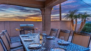 An outdoor dining area with a table set for six, surrounded by chairs, under a pergola with a sunset view. - Havasu Whaler -  Pool, Spa, Game Room, Casita (Lake Havasu City)