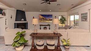 A living room with a sofa, a coffee table, a fireplace, and a ceiling fan. - Havasu Whaler -  Pool, Spa, Game Room, Casita (Lake Havasu City)