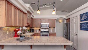 A kitchen with wooden cabinets, a central island with stools, stainless steel appliances, and a decorative wall piece. - Havasu Whaler -  Pool, Spa, Game Room, Casita (Lake Havasu City)