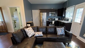 A modern living room with a sectional sofa, ottoman, and a patterned rug. - Cozy cottage-breathtaking sunsets. Lake front. Close to casino & racetrack. (Delanson)