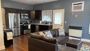 A modern kitchen with stainless steel appliances, a dining area with a black leather couch, and a living room with a patterned rug. - Cozy cottage-breathtaking sunsets. Lake front. Close to casino & racetrack. (Delanson)