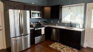 A modern kitchen with stainless steel appliances, dark cabinetry, and a patterned rug. - Cozy cottage-breathtaking sunsets. Lake front. Close to casino & racetrack. (Delanson)