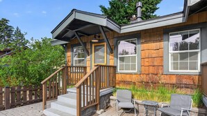 A wooden house with a porch, a staircase, and two chairs.