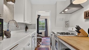 A modern kitchen with white cabinets, a gas stove, a sink, and a patterned rug.