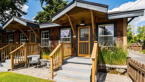 A wooden cabin with a porch, outdoor seating, and a staircase leading to the entrance. - North Sister - Bungalow Charm, Fireplace, Queen bed, Parking (Bend)