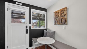 A room with a white door, a bench, a round table, and a wall-mounted sign. - North Sister - Bungalow Charm, Fireplace, Queen bed, Parking (Bend)