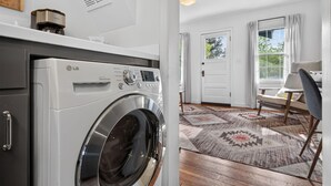 A laundry room with an LG Direct Drive washer and dryer, a white door, a window with curtains, and a patterned rug. - North Sister - Bungalow Charm, Fireplace, Queen bed, Parking (Bend)