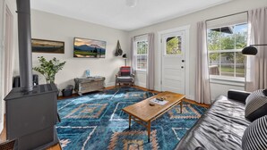 A living room with a fireplace, a sofa, a coffee table, and a view of the outdoors through a window. - Middle Sister - Sweet Bungalow, Queen bed, Parking, Walkable downtown Bend (Bend)