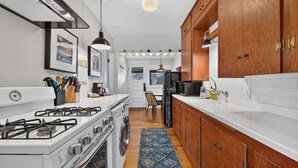A kitchen with a stove, oven, and sink, wooden cabinets, and a patterned rug. - Middle Sister - Sweet Bungalow, Queen bed, Parking, Walkable downtown Bend (Bend)