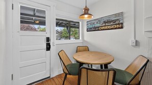 A room with a white door, a round table with four chairs, a hanging pendant light, and a wall-mounted sign that reads 'Celebration in Oregon.' - Middle Sister - Sweet Bungalow, Queen bed, Parking, Walkable downtown Bend (Bend)