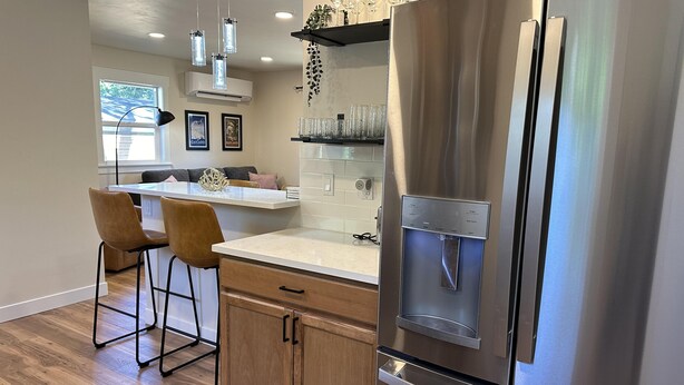A modern kitchen with a stainless steel refrigerator, wooden cabinets, and a bar area with stools.