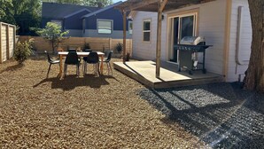 A backyard with a wooden deck, a barbecue grill, and a table with chairs.
