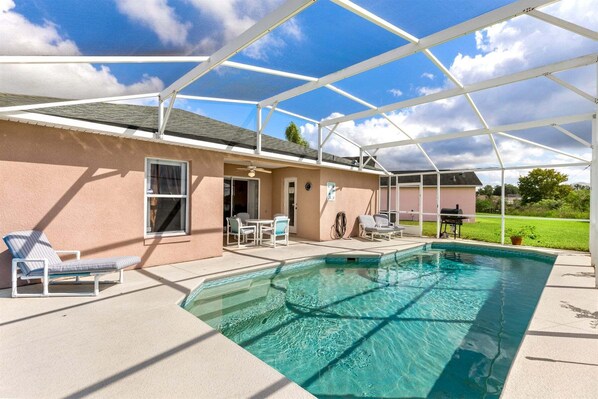 A covered outdoor swimming pool with lounge chairs, a grill, and a patio area.