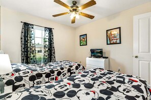 Une chambre avec deux lits, un ventilateur de plafond, une télévision et des œuvres d’art accrochées aux murs.
