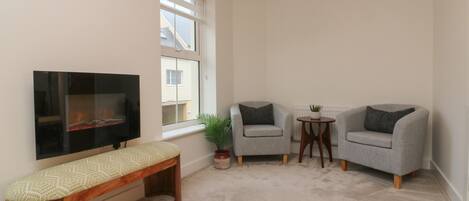A living room with a TV, two grey armchairs, a small round table, a bench, and a potted plant.