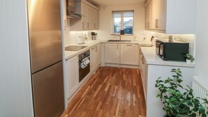 Une cuisine compacte avec des meubles blancs, un réfrigérateur en acier inoxydable, un four à micro-ondes et une fenêtre au-dessus de l’évier.