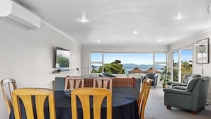 A dining area with a table and chairs, a sofa, and a large window offering a view of the landscape. - Home Away From Home - Taupo (Taupo)