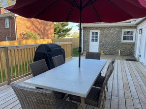 Une terrasse avec une table et des chaises, un barbecue et un grand parasol.